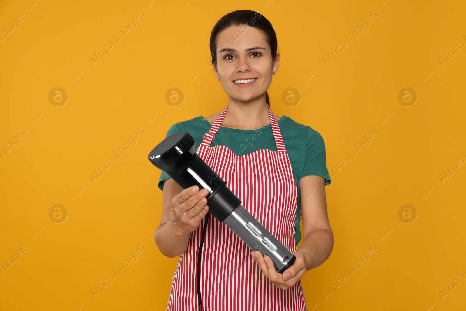 Photo of Beautiful young woman holding sous vide cooker on orange background
