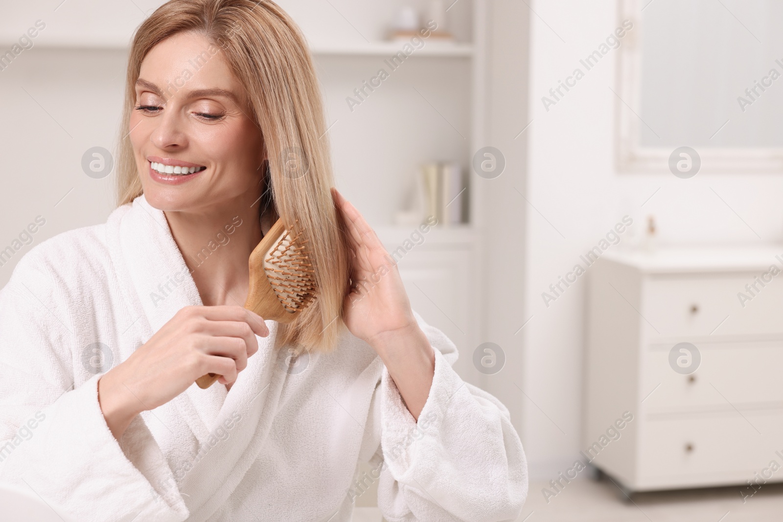 Photo of Beautiful woman brushing her hair in room, space for text