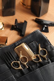 Photo of Hairdresser tools. Professional scissors and combs in leather organizer on wooden table, closeup