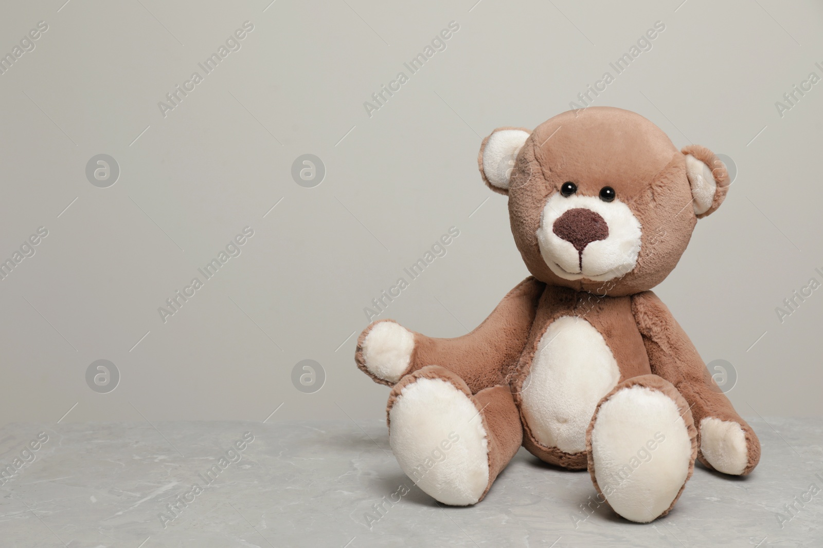 Photo of Cute teddy bear on light grey marble table, space for text