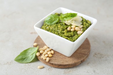 Photo of Bowl with delicious pesto sauce, cheese, pine nuts and basil leaves on light table, closeup