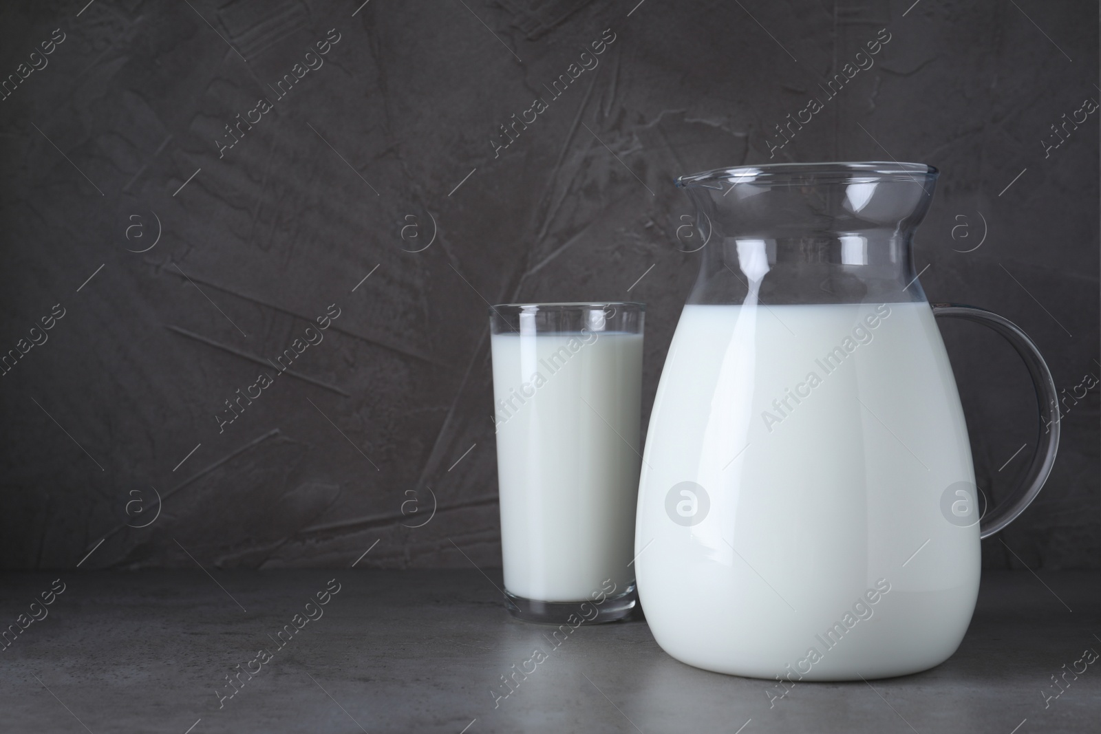 Photo of Jug and glass with fresh milk on grey table. Space for text