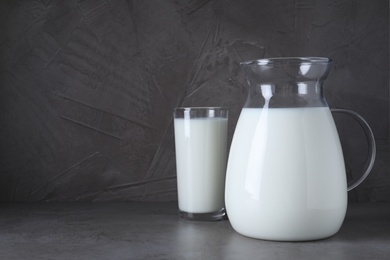 Photo of Jug and glass with fresh milk on grey table. Space for text