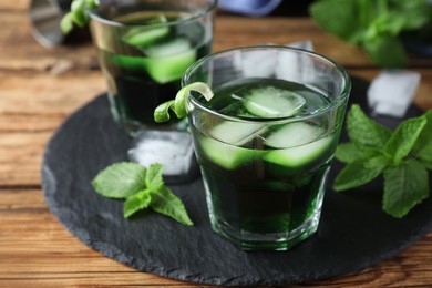 Photo of Delicious mint liqueur with ice cubes and green leaves on wooden table, closeup