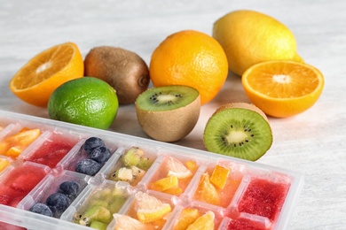 Photo of Ice cubes with fruits and berries in tray near ingredients on light table