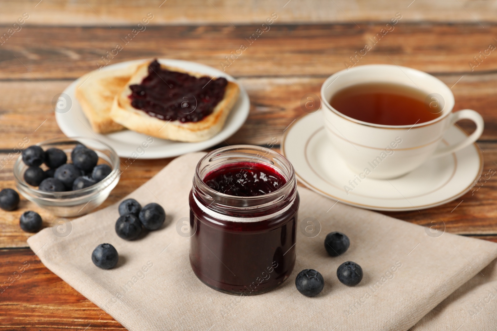 Photo of Delicious blueberry jam, fresh berries and cup of tea on wooden table