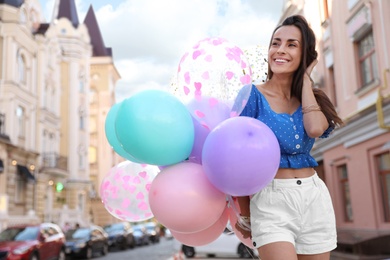 Photo of Beautiful young woman with color balloons on city street