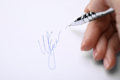 Woman writing her signature with pen on sheet of white paper, closeup