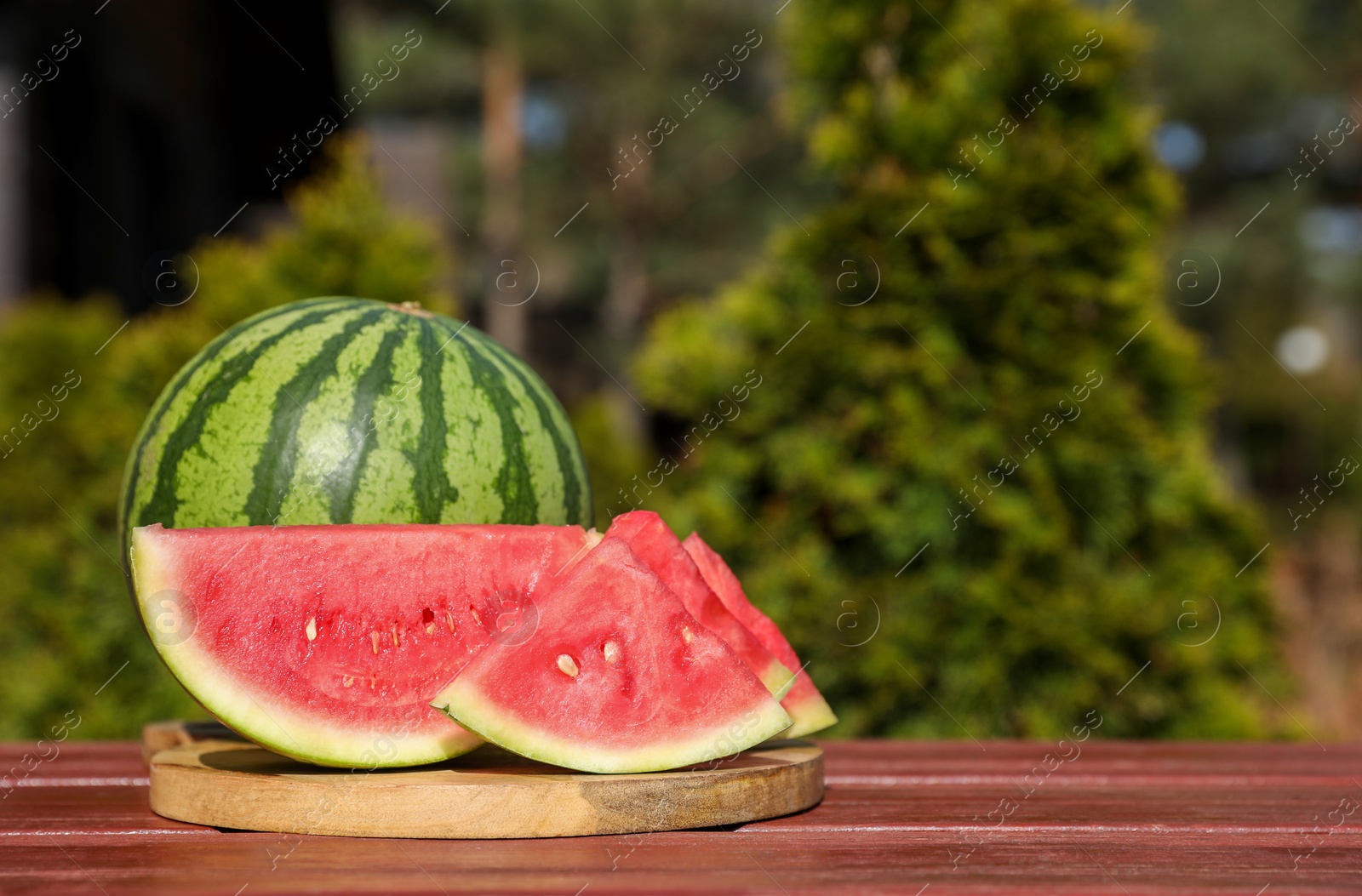 Photo of Delicious cut and whole ripe watermelons on wooden table outdoors, space for text