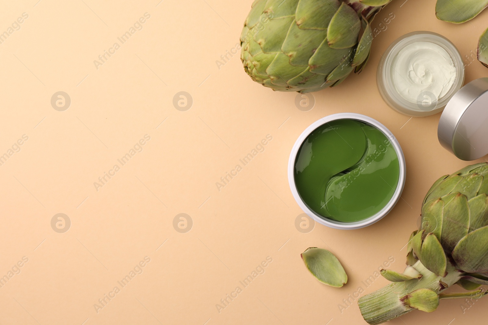 Photo of Package of under eye patches, cosmetic product and artichokes on beige background, flat lay. Space for text