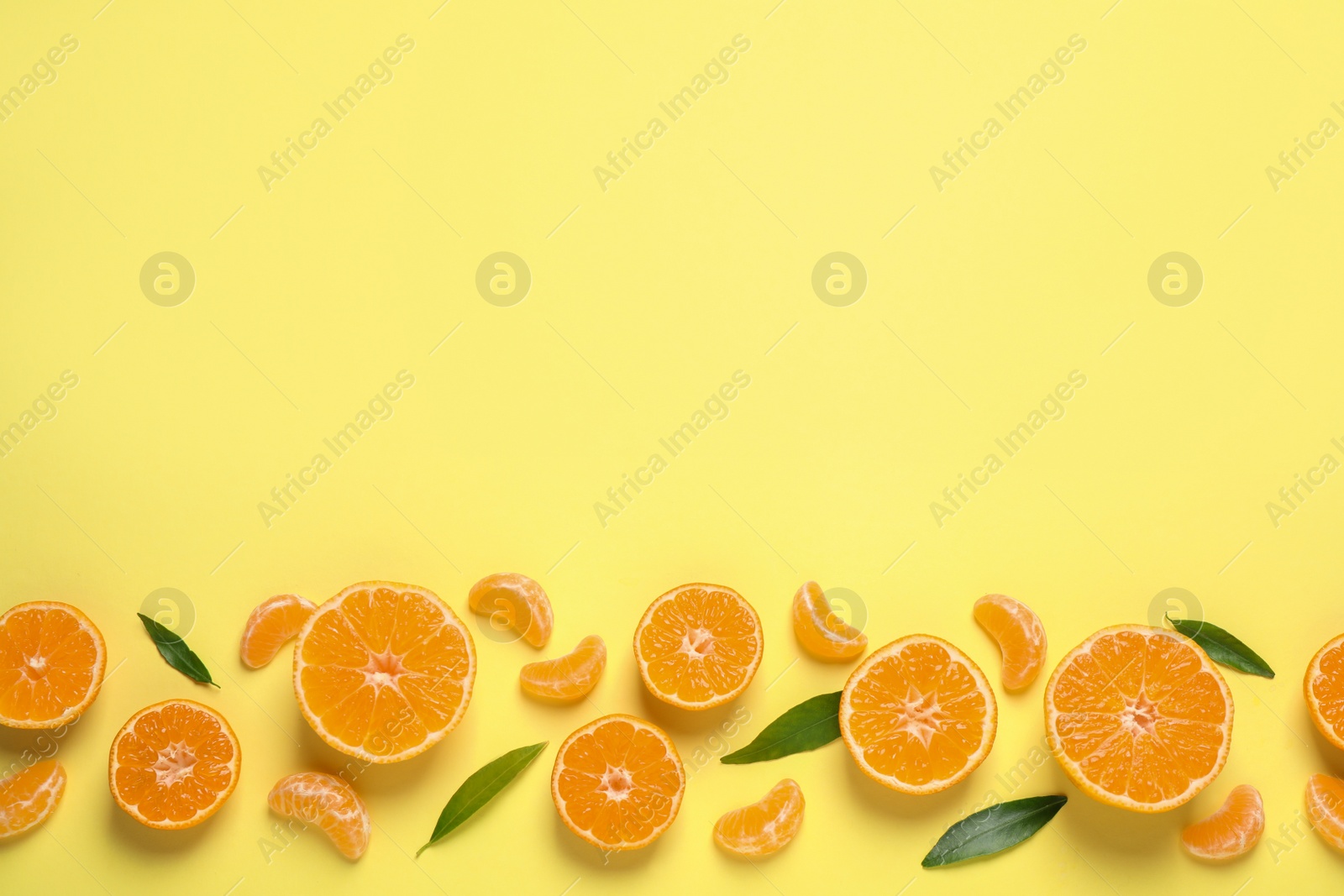 Photo of Flat lay composition with fresh ripe tangerines and leaves on light yellow background, space for text. Citrus fruit