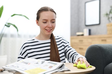 Photo of Woman cleaning wooden coffee table with rag at home