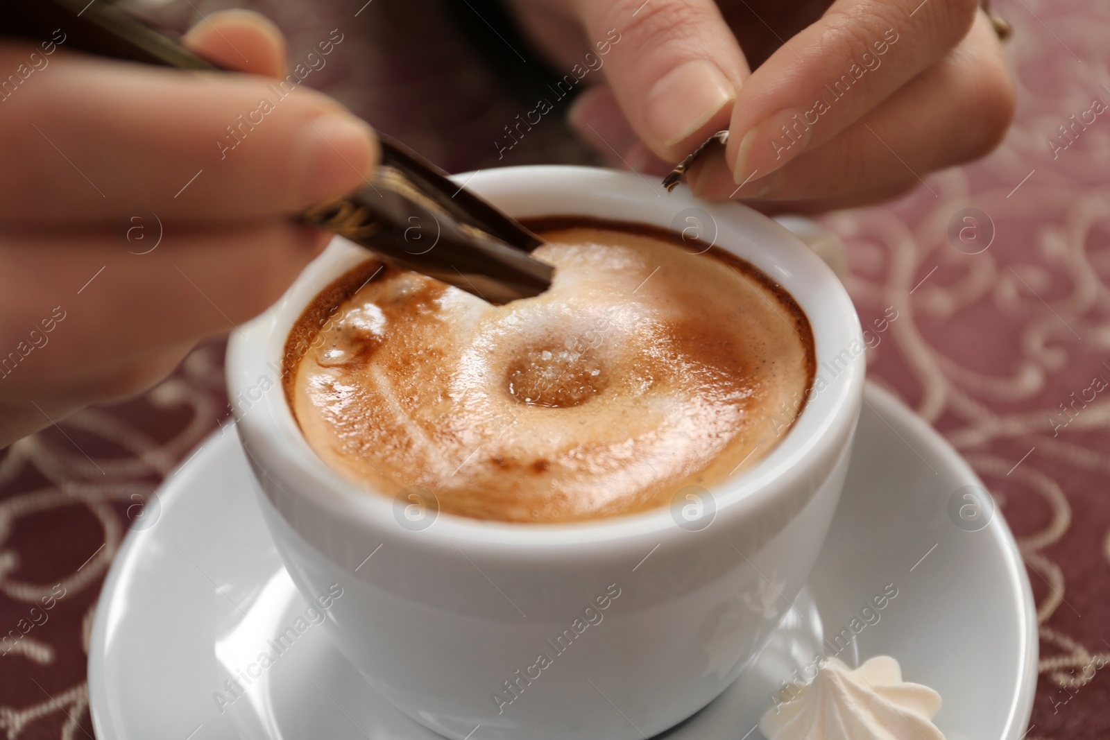 Photo of Young woman adding sugar to delicious coffee at table, closeup