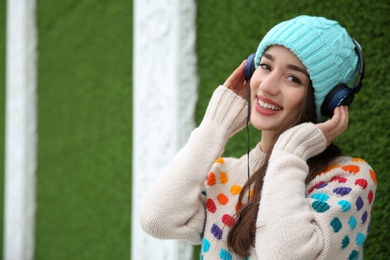 Photo of Beautiful young woman listening to music with headphones near grass wall. Space for text