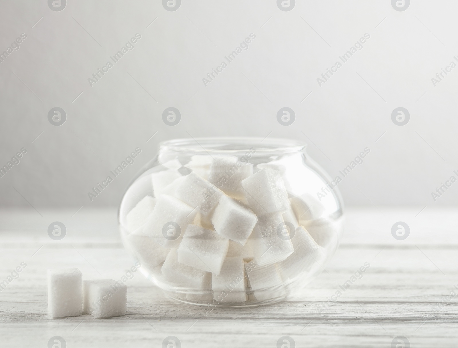 Photo of Refined sugar cubes in glass bowl on white wooden table