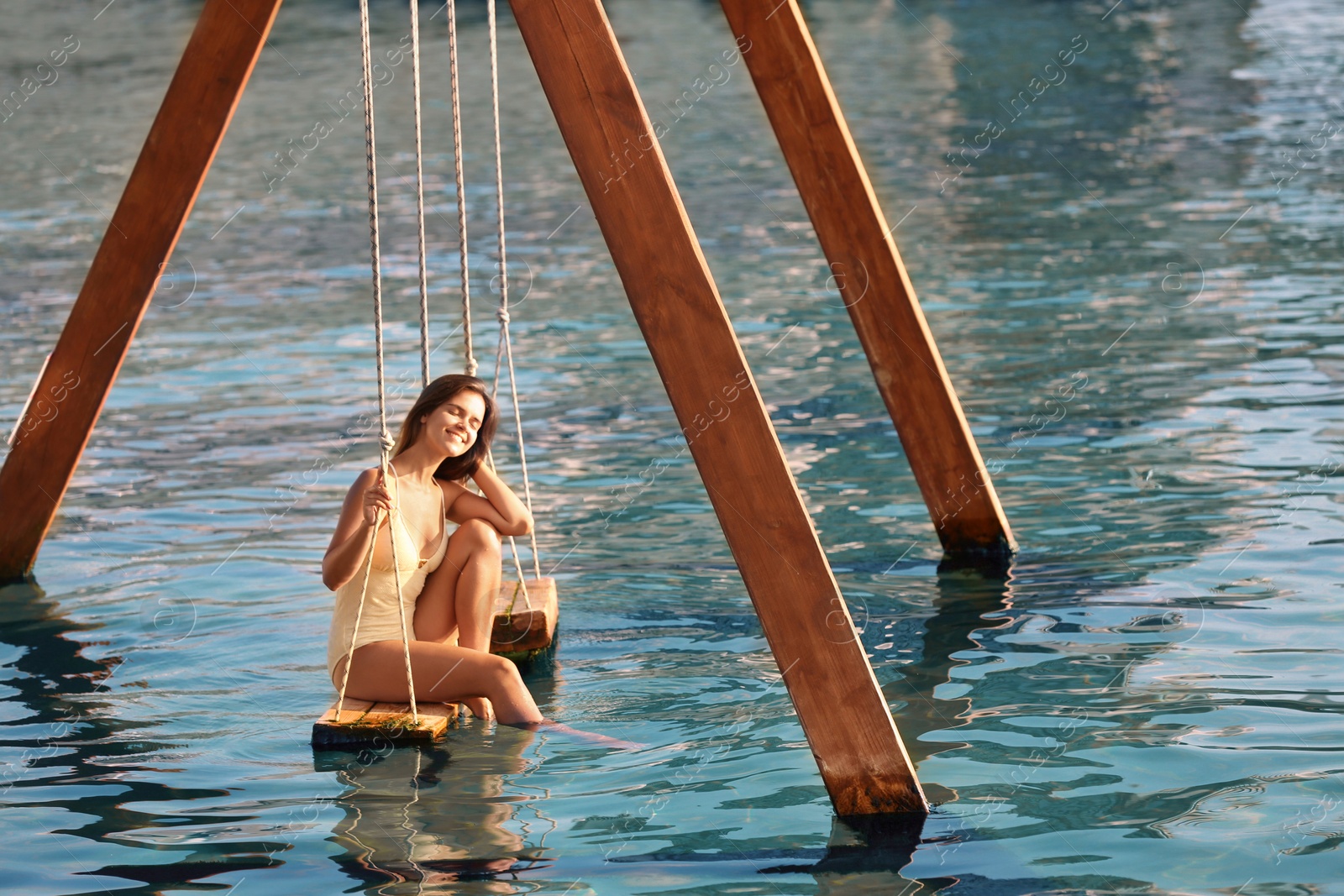 Photo of Young woman on swing over water on sunny day