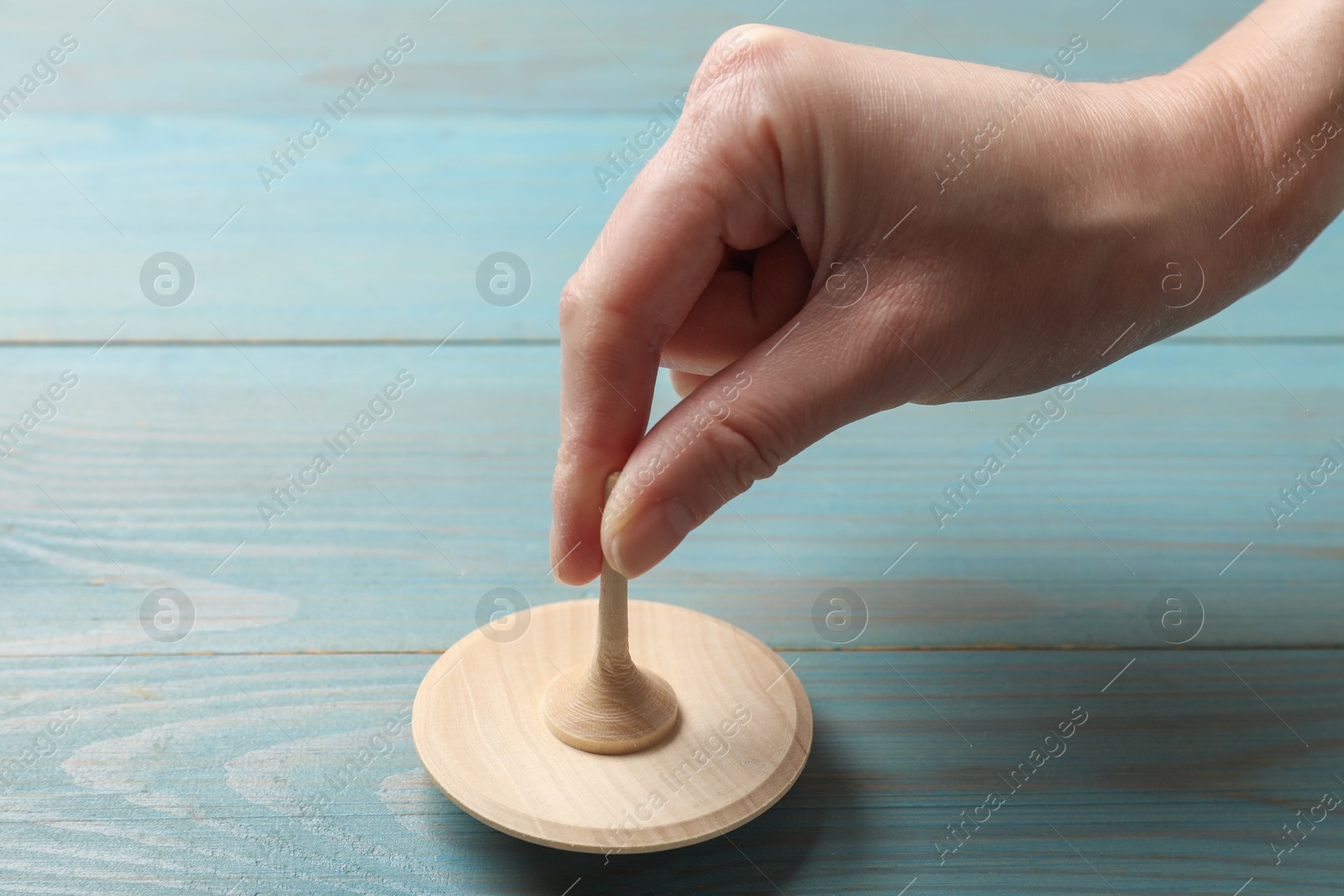 Photo of Woman playing with spinning top at light blue wooden table, closeup