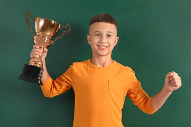 Happy boy with golden winning cup on near chalkboard