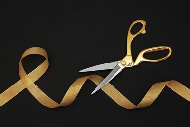 Gold satin ribbon and scissors on black background, flat lay