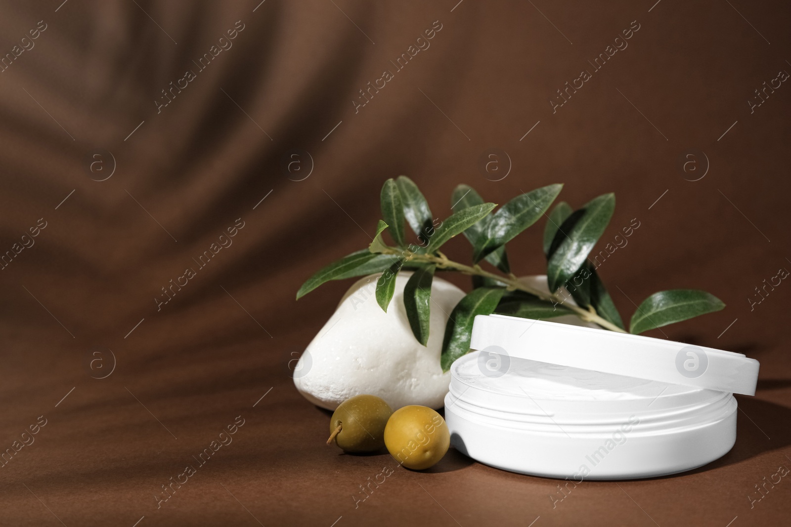 Photo of Jar of natural cream, stone and olives on brown background, space for text. Cosmetic products