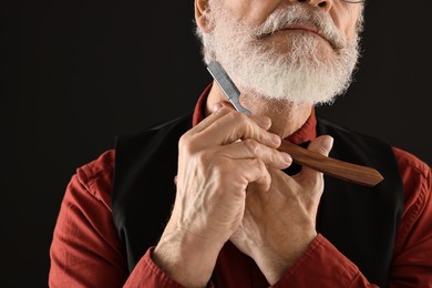 Photo of Man shaving beard with blade on black background, closeup