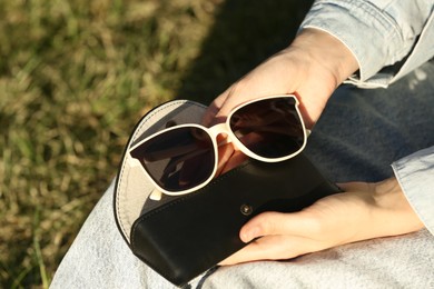 Woman holding sunglasses and case outdoors on sunny day, closeup