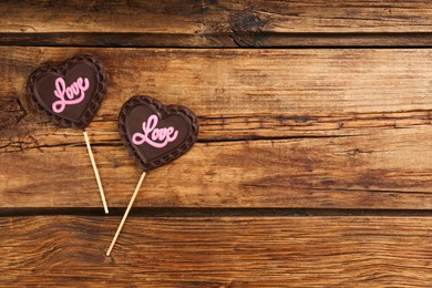 Chocolate heart shaped lollipops with word Love on wooden table, flat lay. Space for text