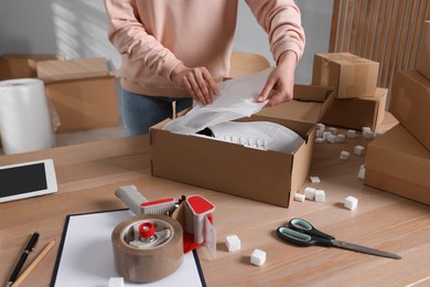 Photo of Seller packing shoes into cardboard box at table in office, closeup. Online store