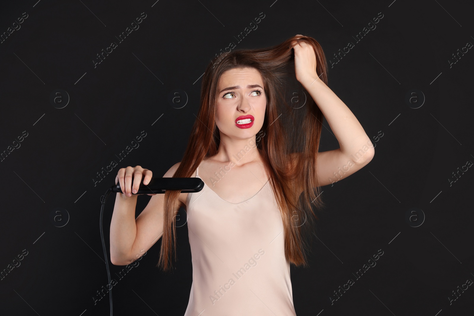 Photo of Stressed young woman with flattening iron on black background. Hair damage