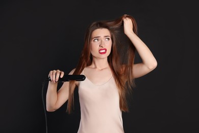 Photo of Stressed young woman with flattening iron on black background. Hair damage