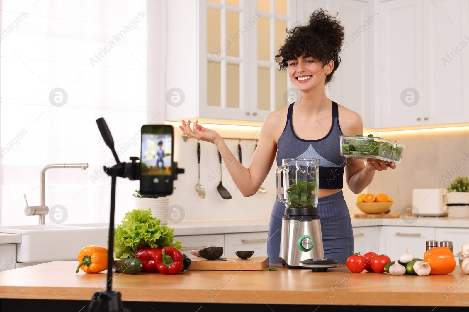 Photo of Smiling food blogger explaining something while recording video in kitchen