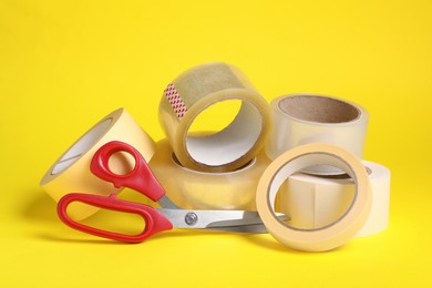 Photo of Rolls of adhesive tape and scissors on yellow background