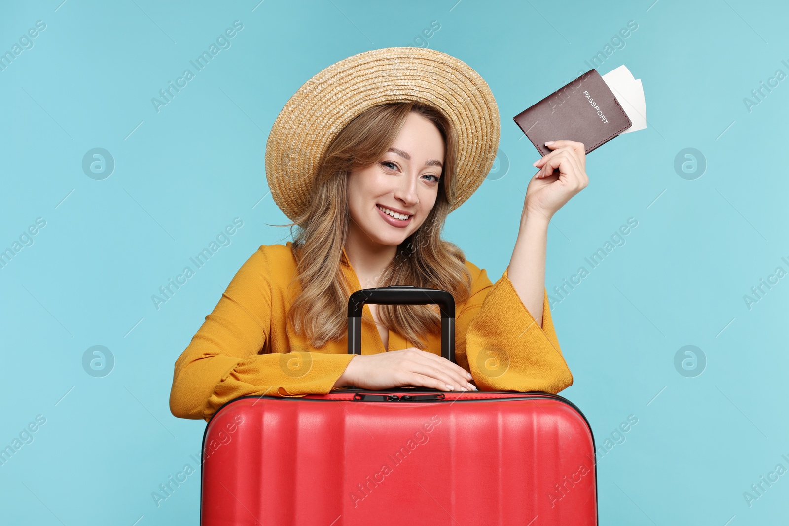 Photo of Happy young woman with passport, ticket and suitcase on light blue background