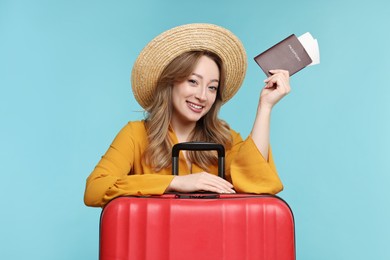 Happy young woman with passport, ticket and suitcase on light blue background