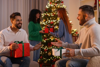 Photo of Christmas celebration. Happy friends exchanging gifts at home, selective focus