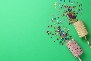 Photo of Colorful confetti and party crackers on green background, flat lay. Space for text