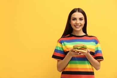 Young woman with tasty burger on color background. Space for text