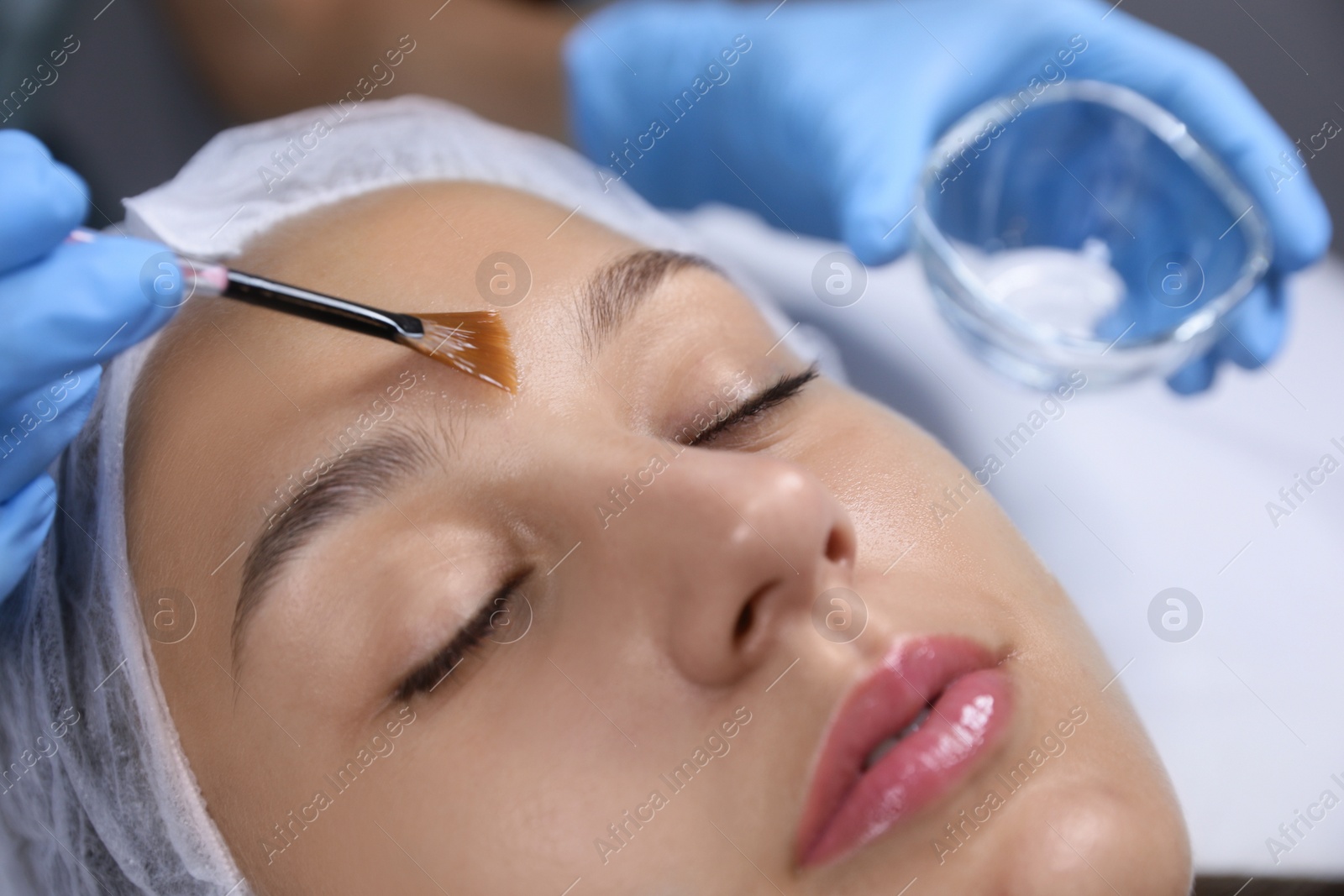 Photo of Cosmetologist applying chemical peel product on client's face in salon, closeup