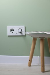 Smartphone plugged into electric socket on light green wall