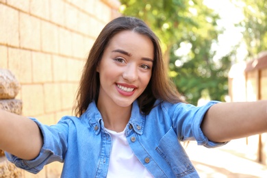 Photo of Young woman taking selfie outdoors on sunny day