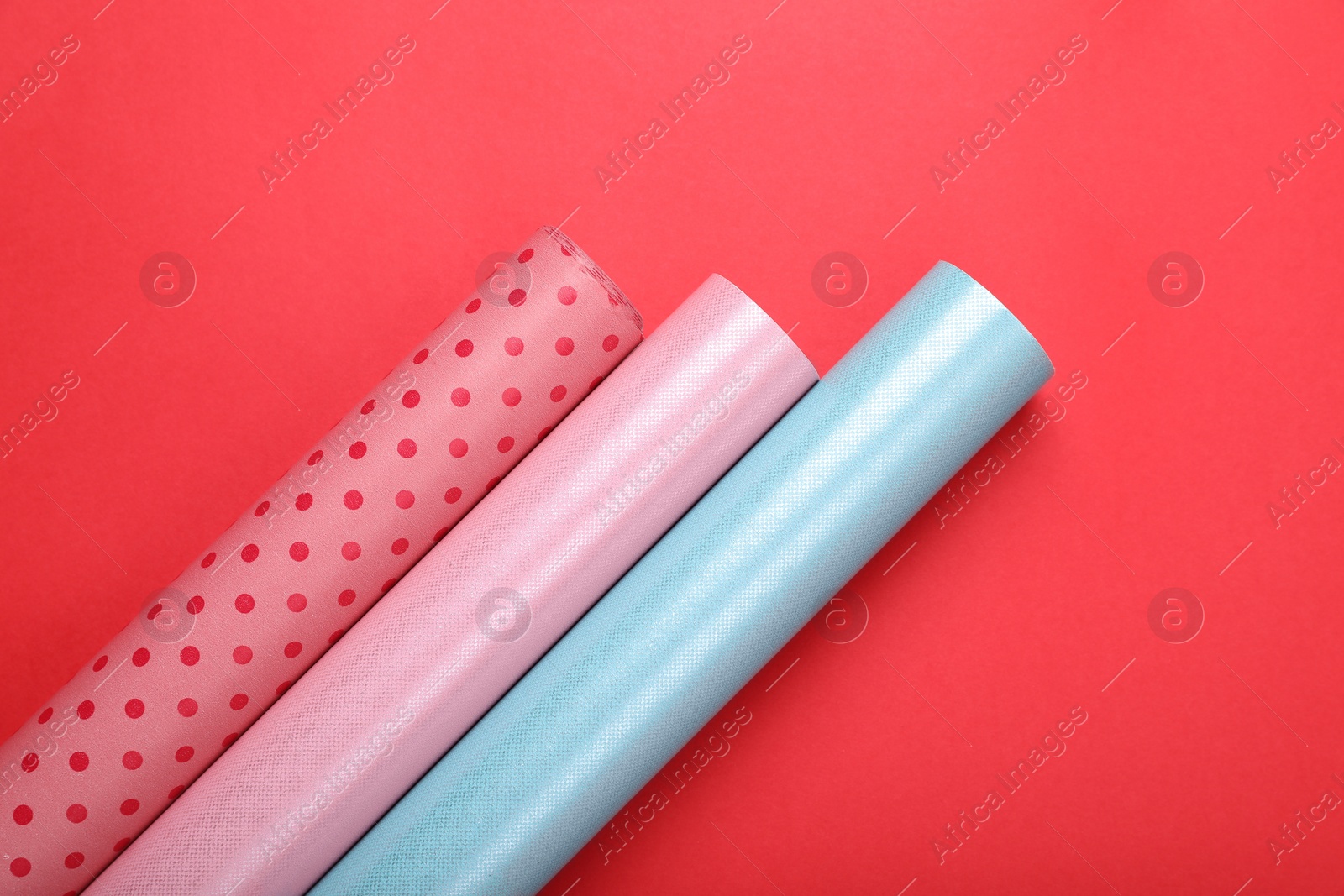 Photo of Rolls of colorful wrapping papers on red background, flat lay