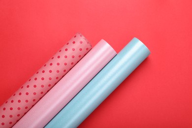 Photo of Rolls of colorful wrapping papers on red background, flat lay