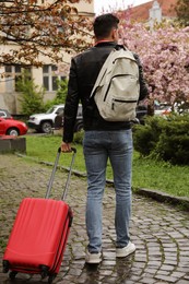Photo of Tourist with stylish suitcase and backpack on city street, back view
