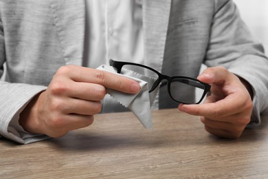 Photo of Man wiping glasses with microfiber cloth at wooden table, closeup