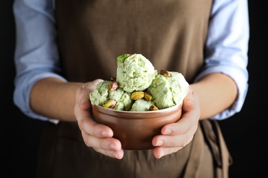 Woman holding bowl full of pistachio ice cream on black background, closeup