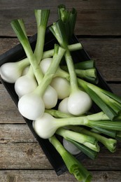 Photo of Black crate with green spring onions on wooden table, top view