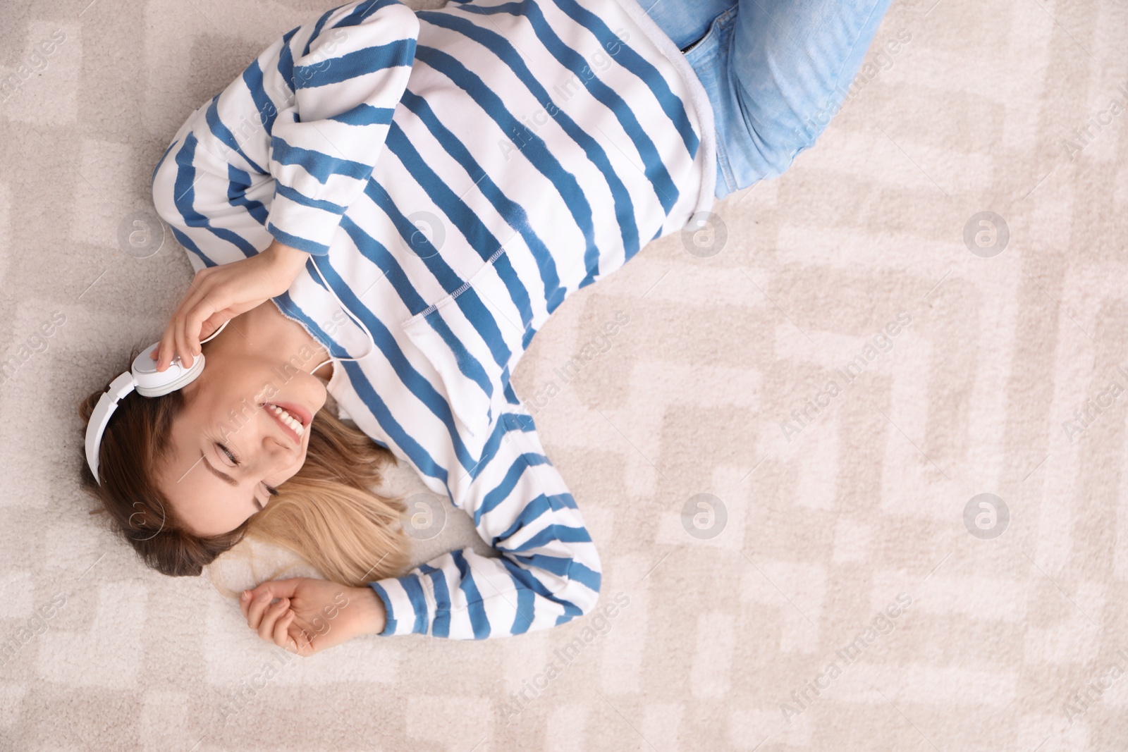 Photo of Young woman in headphones enjoying music on floor, top view with space for text