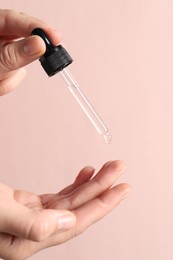 Photo of Woman applying cosmetic serum onto fingers on light pink background, closeup