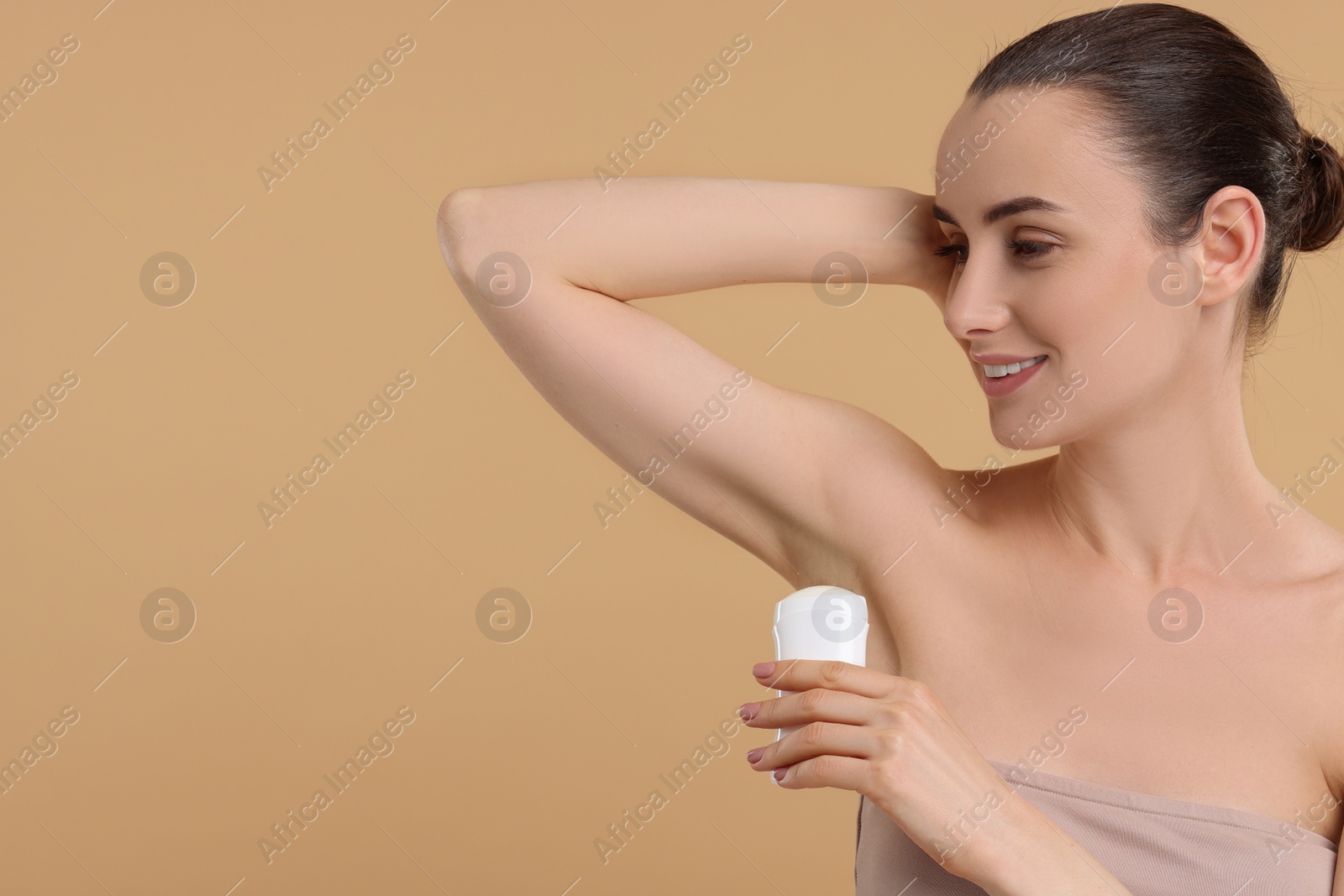 Photo of Beautiful woman applying deodorant on beige background, space for text