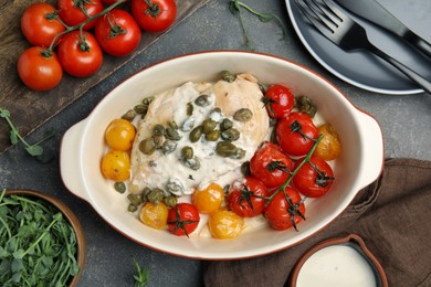 Photo of Delicious baked chicken fillet with capers, sauce and tomatoes in baking dish on grey table, flat lay